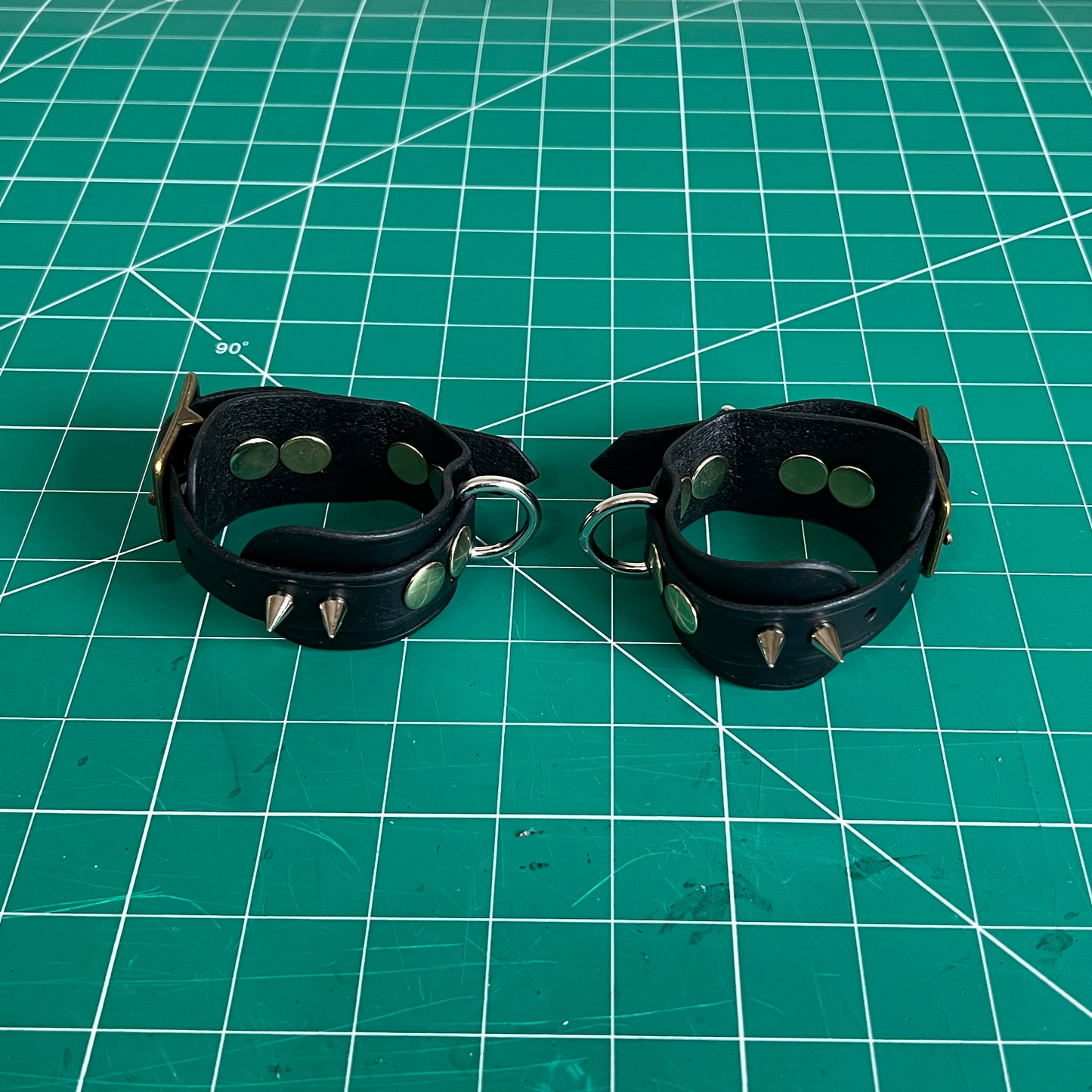 Black leather wrist cuffs with studs on a green cutting mat