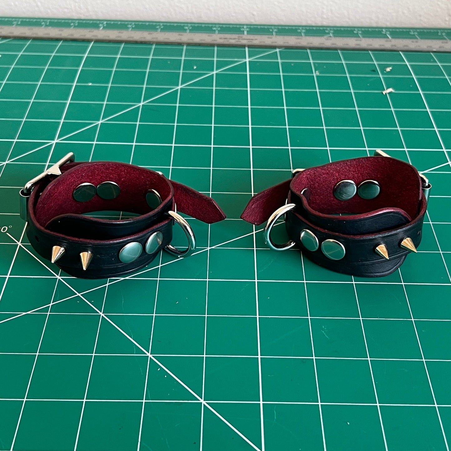 Two leather cuffs with studs on a green cutting mat.