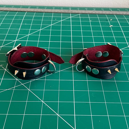 Two leather cuffs with studs on a green cutting mat.