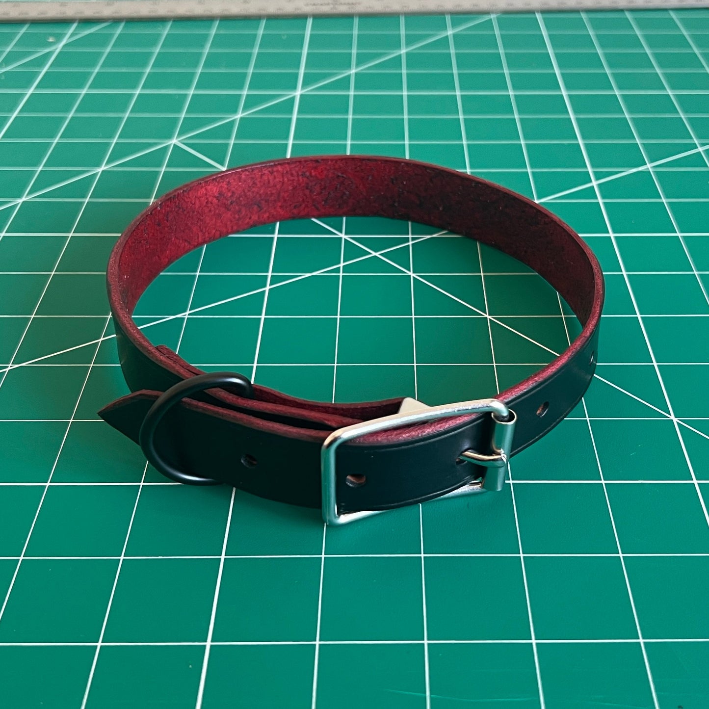 Red and black leather collar on a green cutting mat