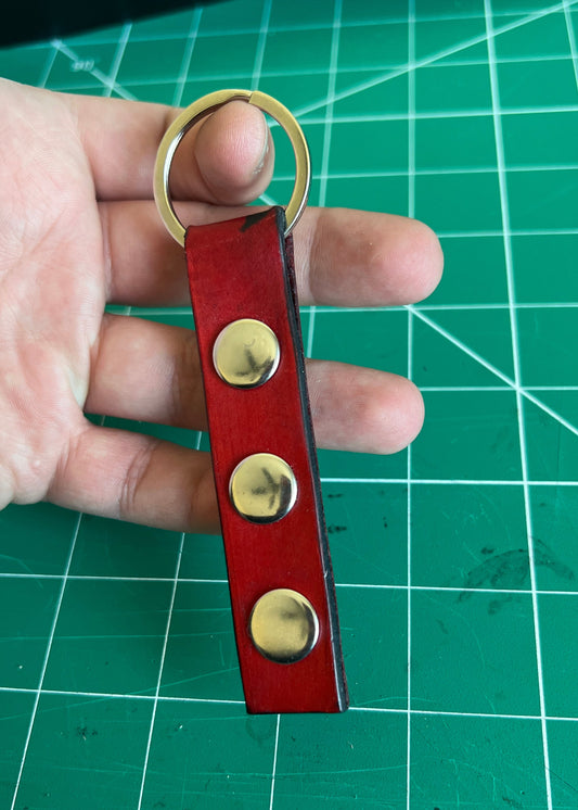 Red leather keychain with brass rivets held by a hand on a green cutting mat.
