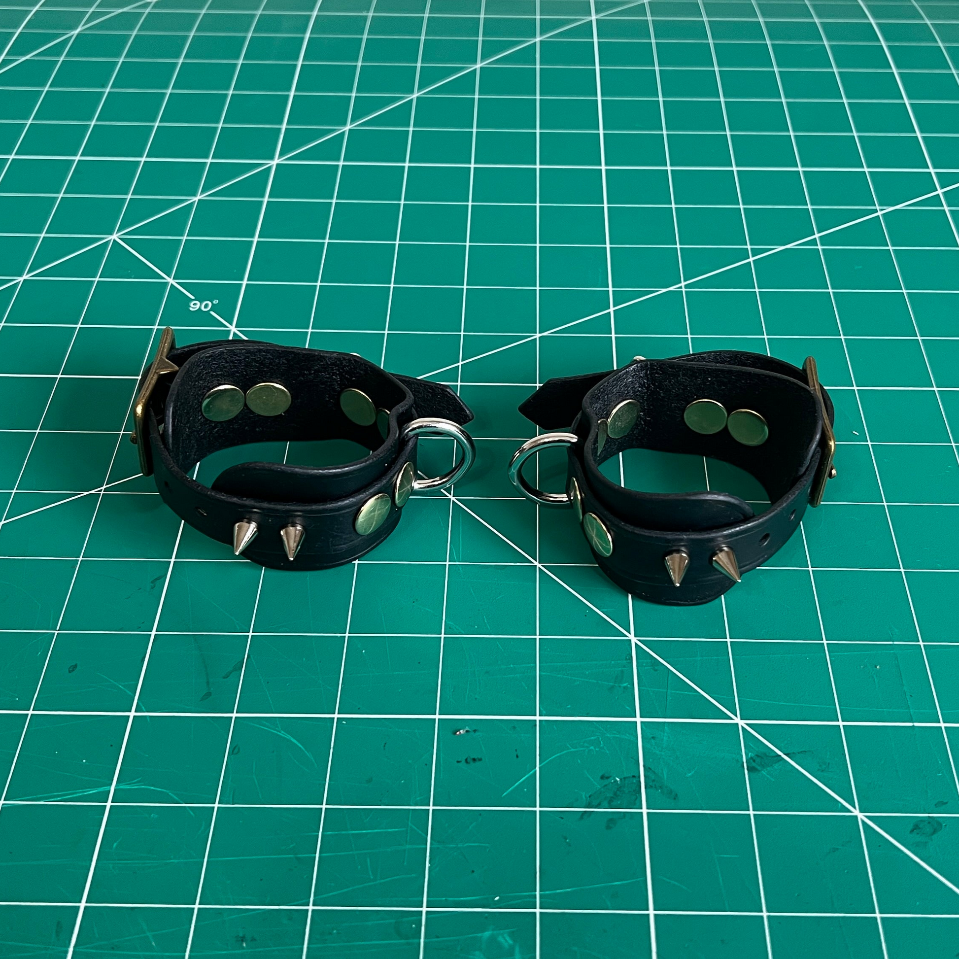 Black leather wrist cuffs with studs on a green cutting mat